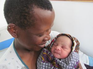 A women carying a little baby sleeping in a blanquet, the mother looks at the baby and smile.