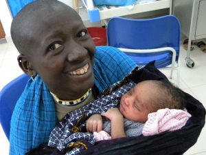 A women with a big smile is carying a little baby in a blanquet